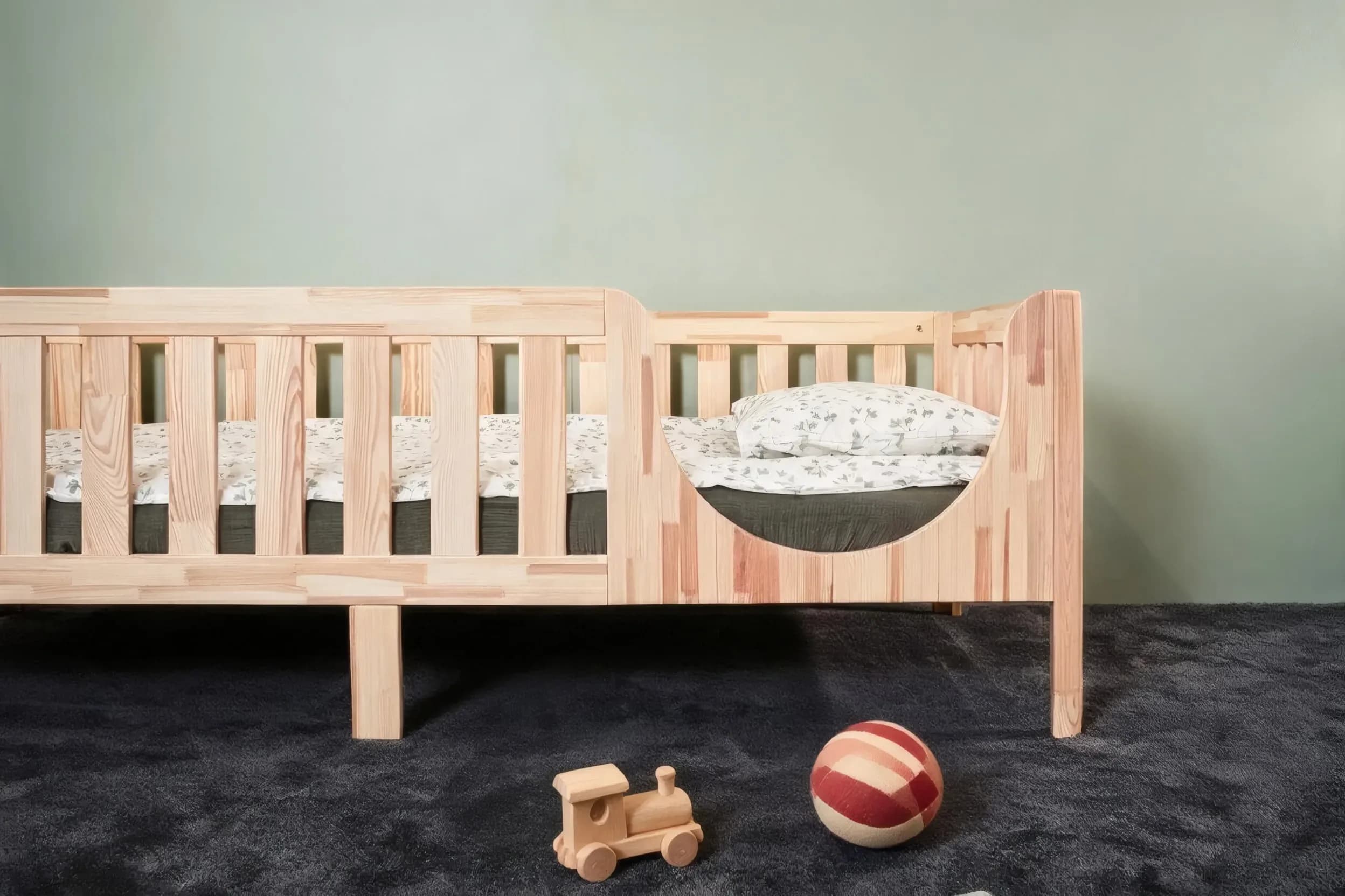 Bett auf Beinen mit abgerundetem Einstieg und Holzspielzeug am Boden, nähere Vorderansicht