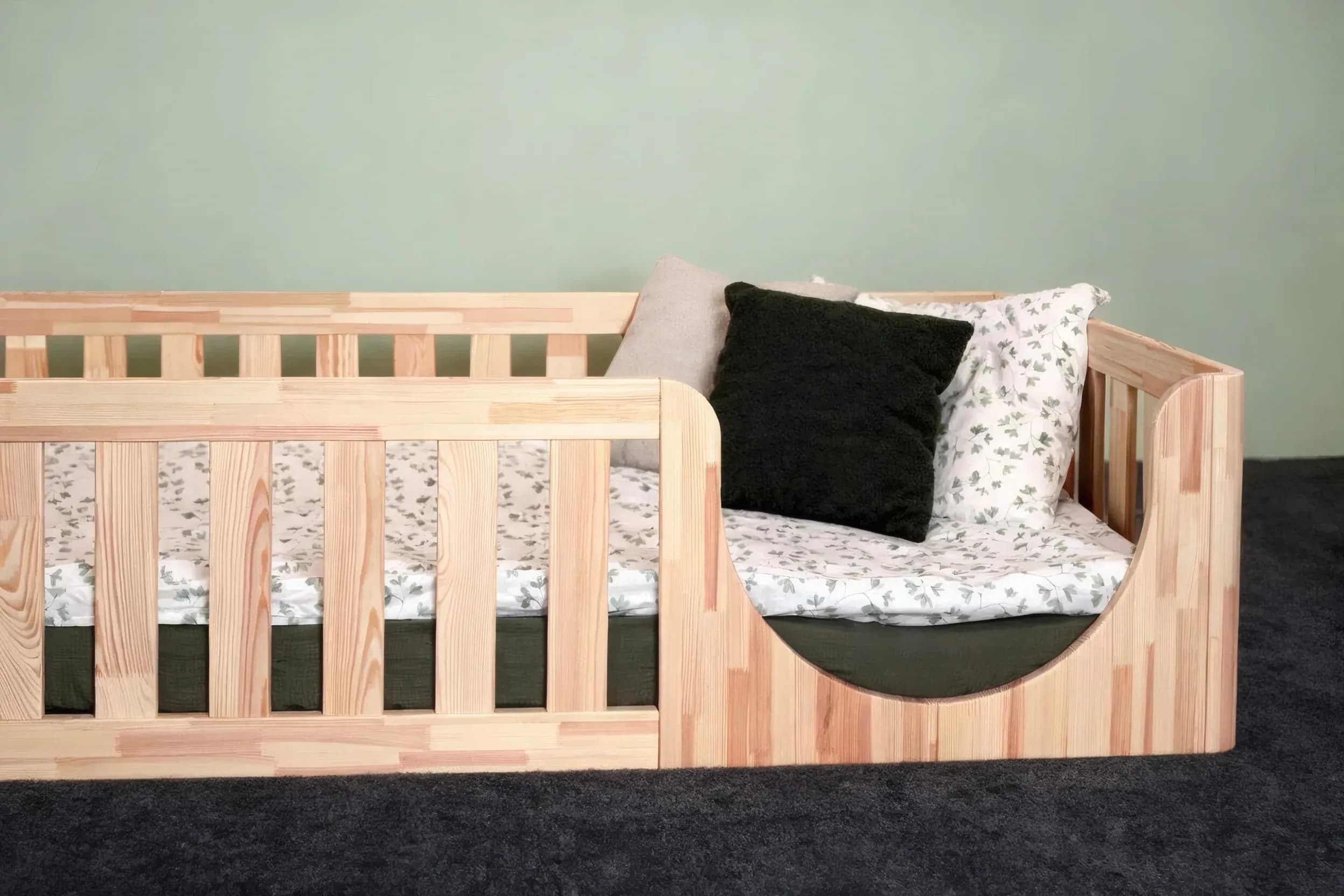 Montessori-Bodenbett mit abgerundetem Einstieg und dunkelgrünem Kissen, Schrägansicht