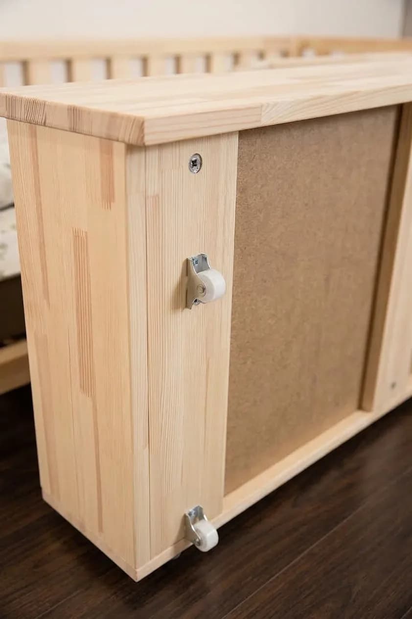 Close-up bottom view of a natural solid wood Montessori bed storage drawer showing sturdy wheels and construction