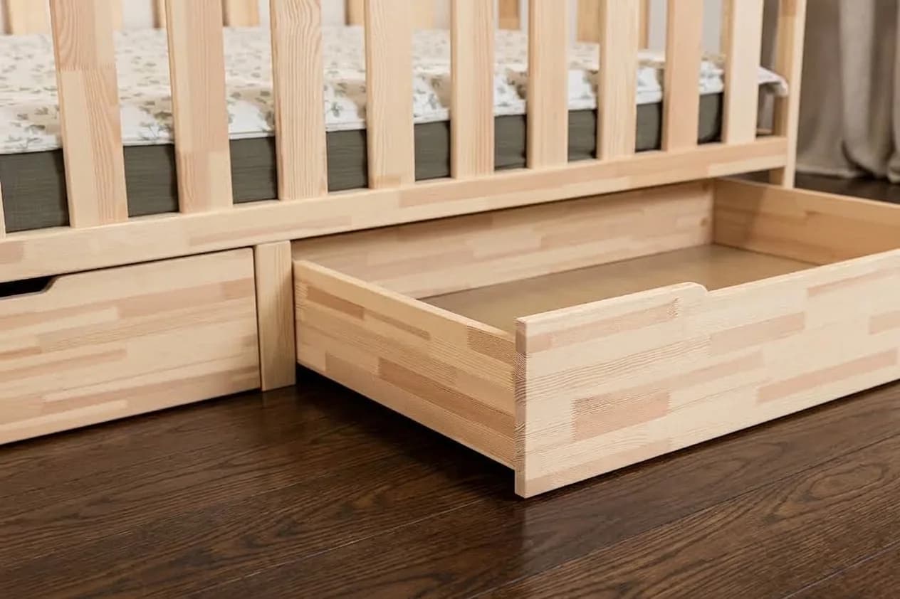 Close-up of natural solid wood Montessori bed frame details showing pull-out drawer mechanism on wheels and sturdy wooden legs
