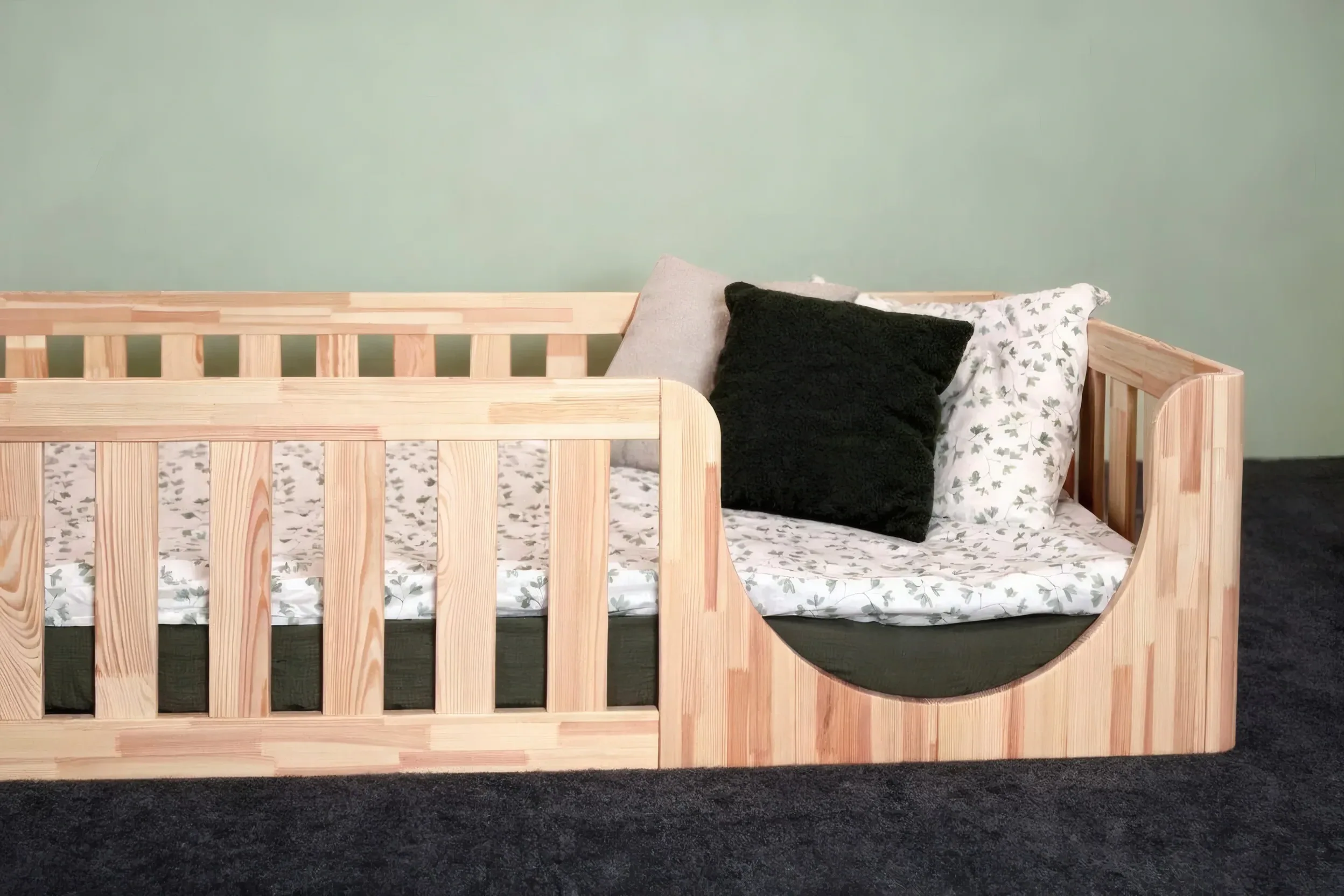 Cama Montessori con entrada semicircular y cojín verde oscuro, vista en ángulo