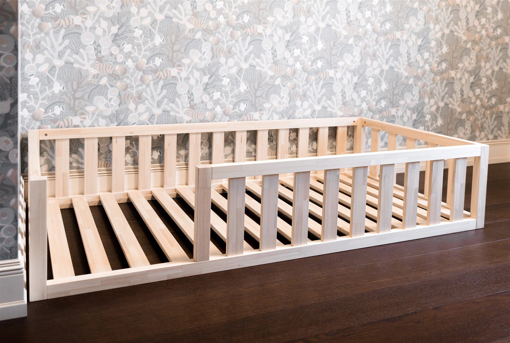 Cama de suelo Montessori de pino natural con barandillas y lamas de madera, vista en ángulo