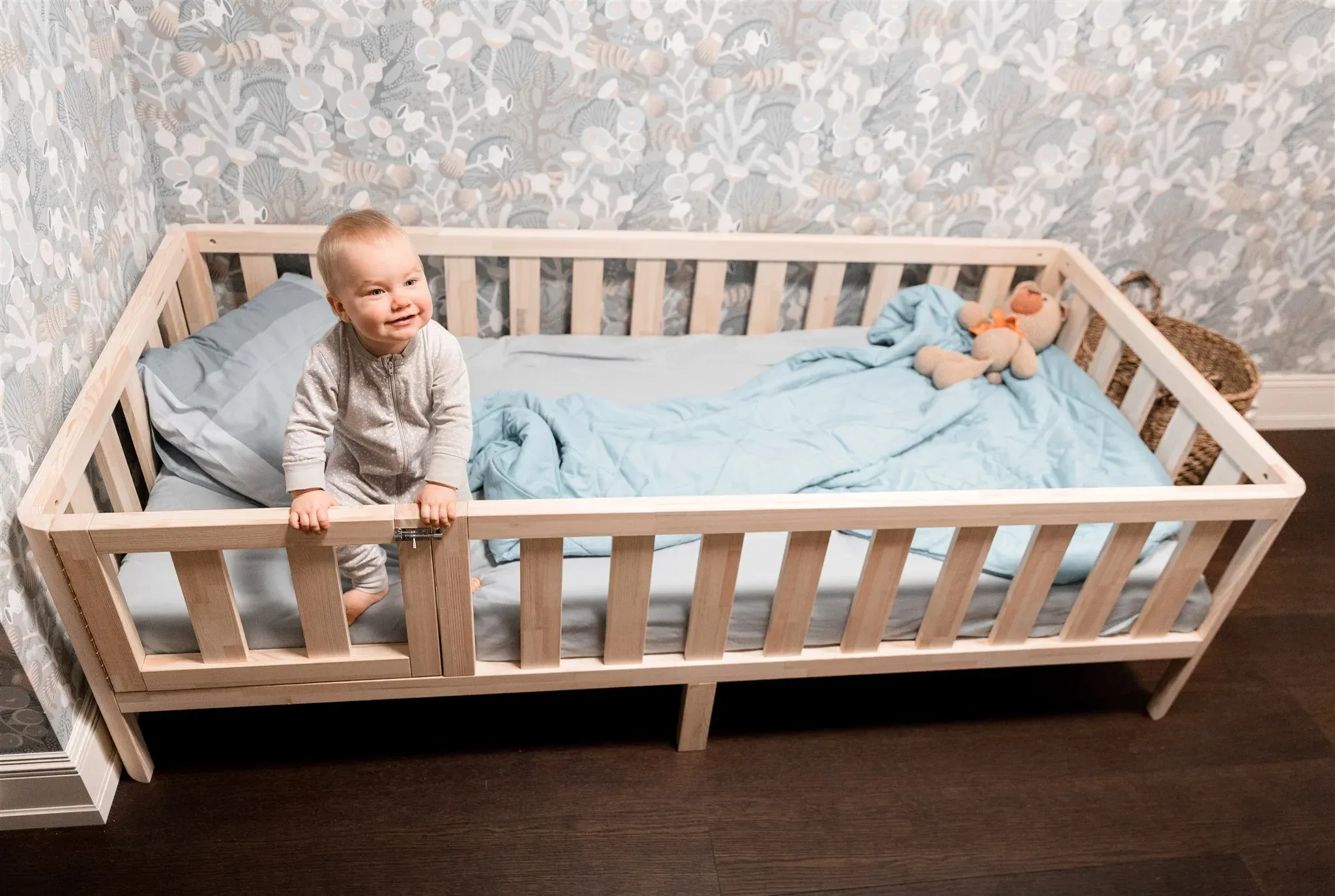 Bambino sorridente in un letto Montessori in pino con piedini e cancelletto