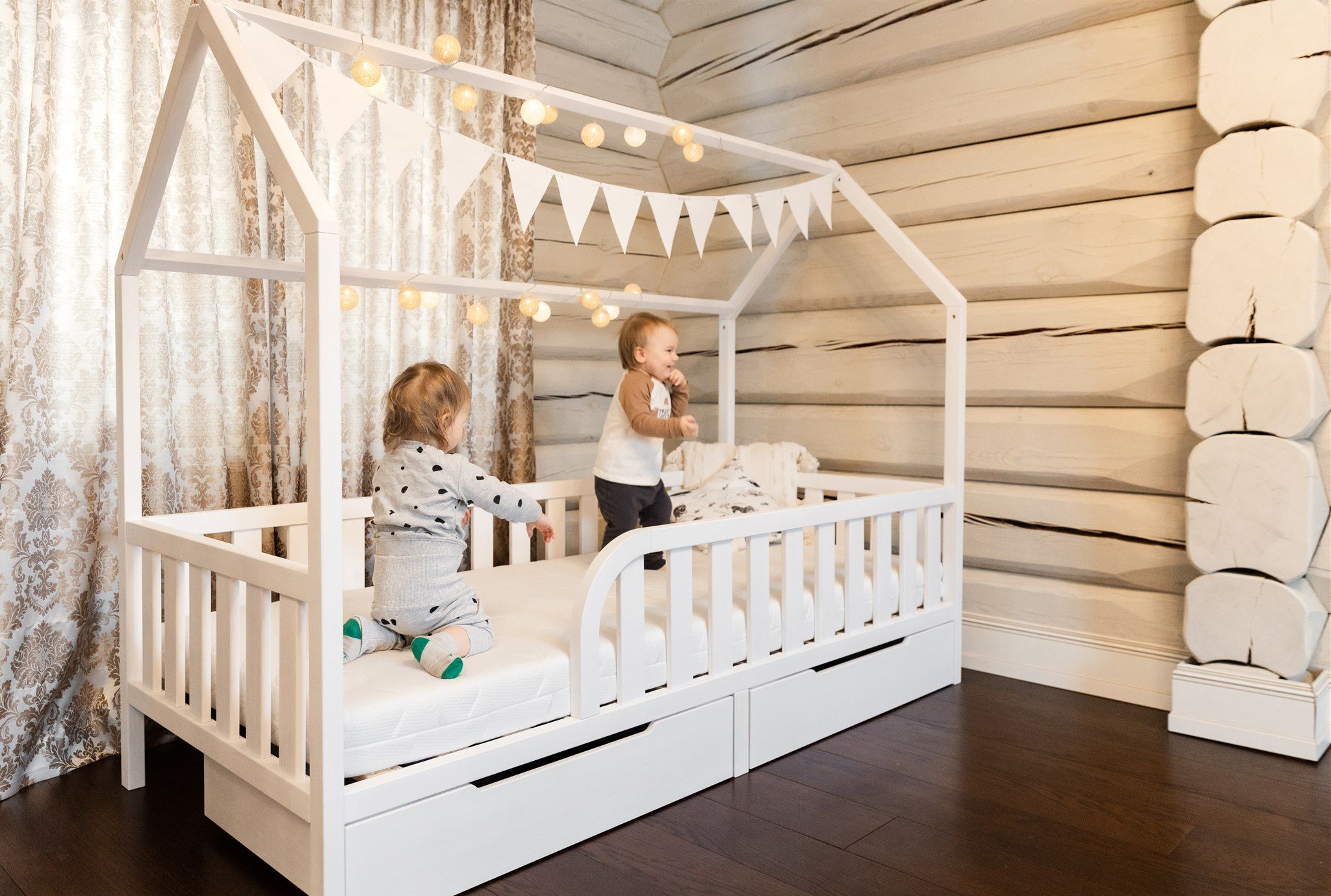 Dos niños en una cama casita Montessori blanca con cajones y entrada redondeada