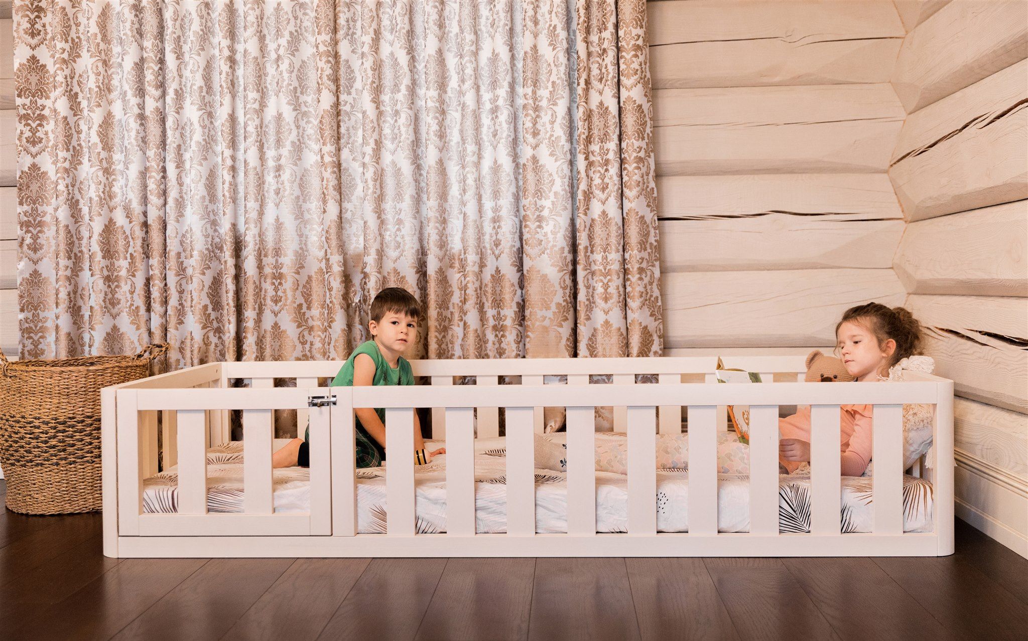 Dwoje dzieci w białym łóżku podłogowym Montessori z drzwiczkami zabezpieczającymi